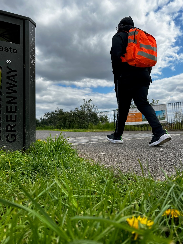 A young black man walks on a green area in East London. The pictures help the reader to understand the impact of migration in migrant's mental health. 